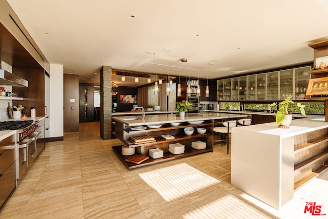 interior space with a large island with sink, sink, ornate columns, and appliances with stainless steel finishes