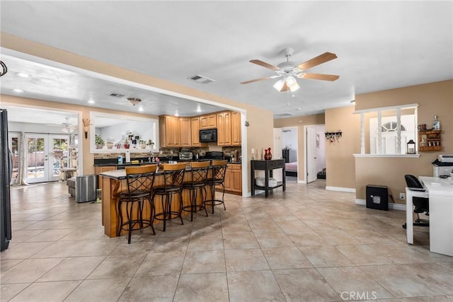 kitchen featuring a breakfast bar area, light tile patterned floors, ceiling fan, black appliances, and french doors