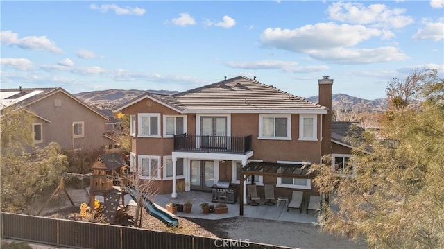 back of house with a playground, a mountain view, and a balcony