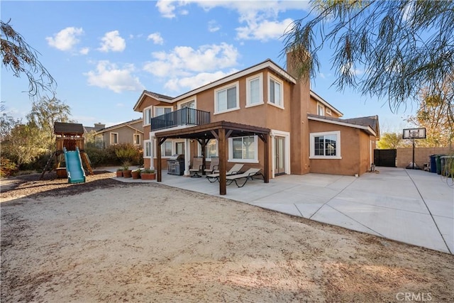 rear view of house featuring a patio, a playground, and a balcony