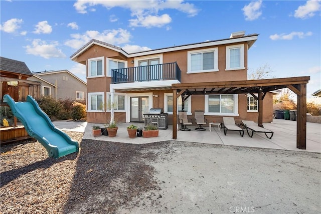 rear view of property featuring a pergola, a playground, a patio, and a balcony