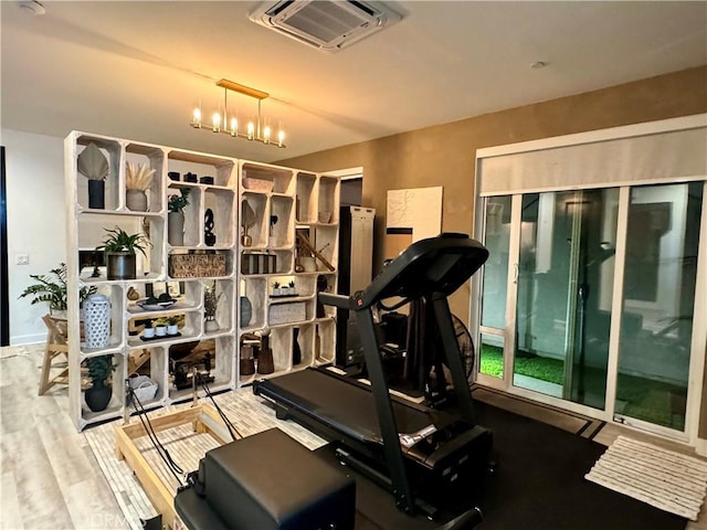 workout room with light wood-type flooring and an inviting chandelier