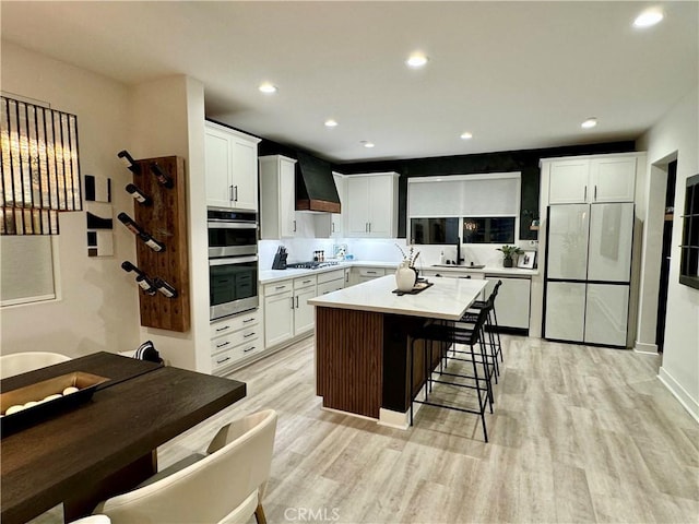 kitchen with custom exhaust hood, light hardwood / wood-style floors, fridge, and a center island