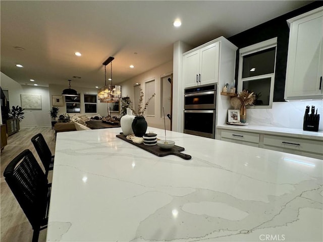 kitchen with light stone counters, stainless steel double oven, white cabinets, and hanging light fixtures