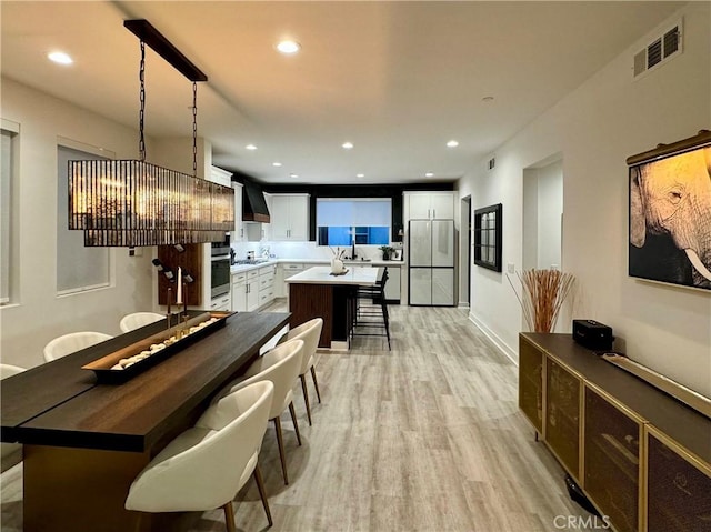 interior space with oven, a center island, fridge, white cabinetry, and hanging light fixtures