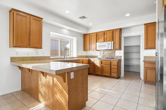 kitchen with backsplash, a kitchen breakfast bar, stainless steel fridge, light tile patterned floors, and kitchen peninsula