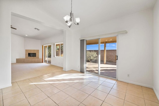 interior space featuring a tile fireplace, light carpet, a healthy amount of sunlight, and an inviting chandelier