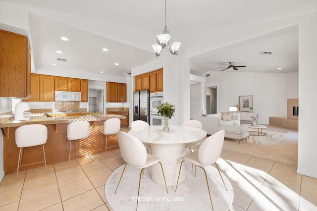 dining area with a tile fireplace, ceiling fan with notable chandelier, light tile patterned floors, and vaulted ceiling