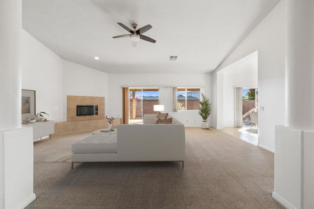 living room with a tiled fireplace, light carpet, and vaulted ceiling