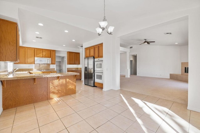 kitchen with white appliances, light carpet, a kitchen breakfast bar, ceiling fan with notable chandelier, and kitchen peninsula