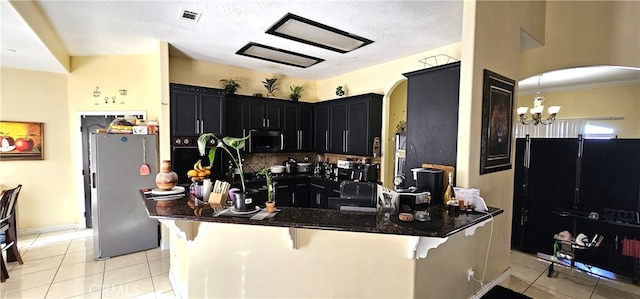 kitchen featuring stainless steel appliances, a notable chandelier, dark stone counters, a breakfast bar area, and light tile patterned floors