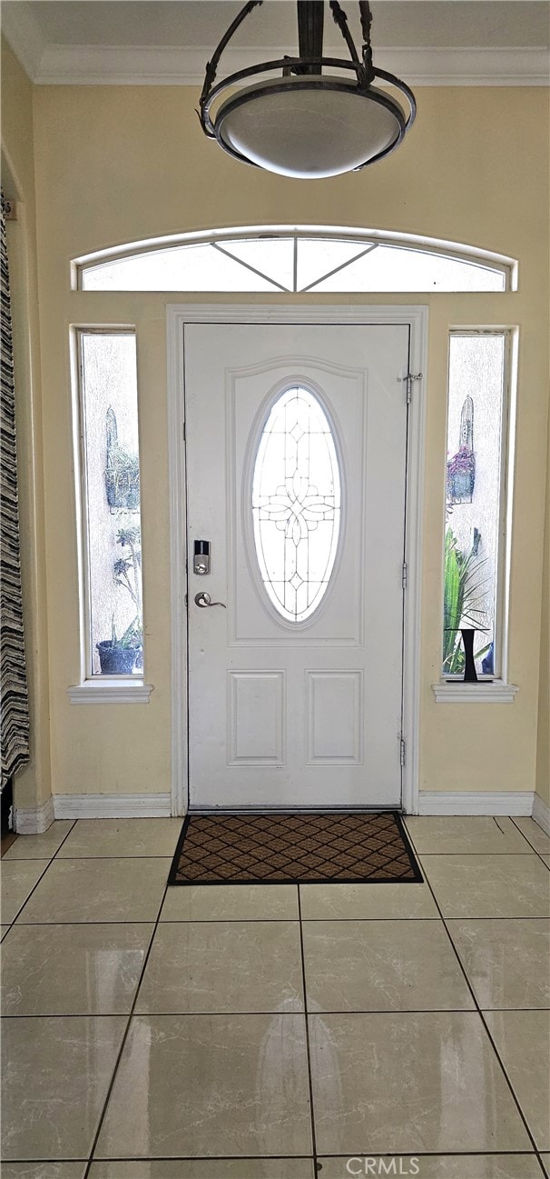 tiled entryway featuring crown molding and a notable chandelier