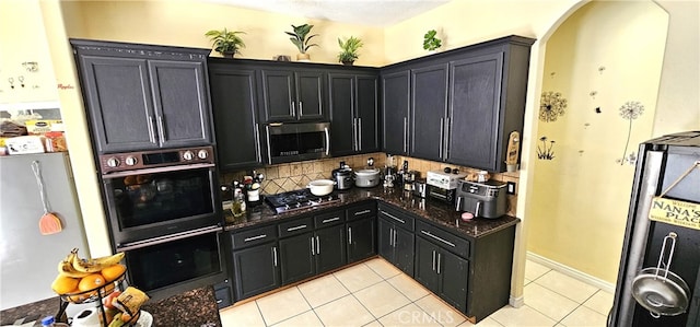 kitchen featuring appliances with stainless steel finishes, backsplash, light tile patterned floors, and dark stone countertops