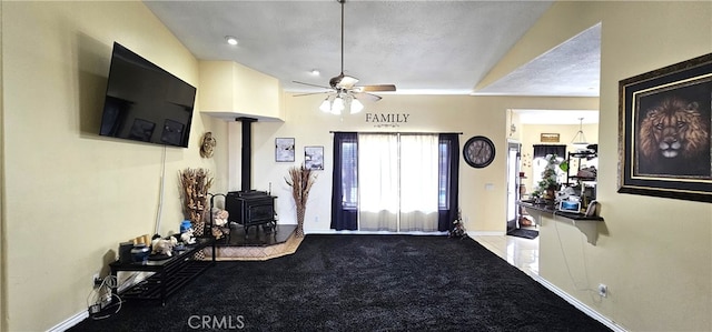 carpeted living room with ceiling fan, a wood stove, and a textured ceiling