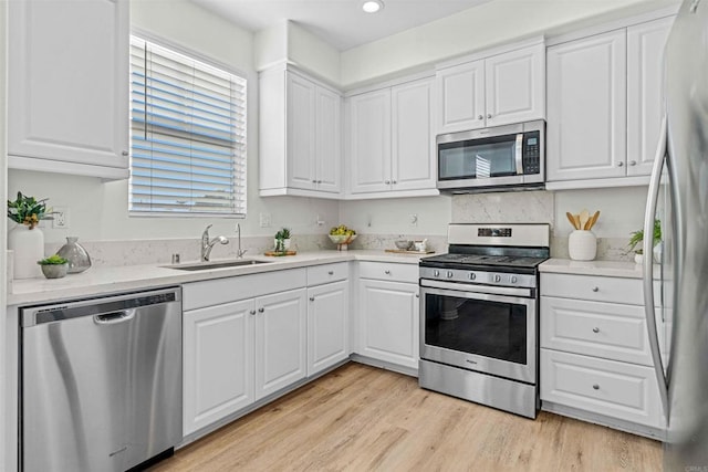 kitchen featuring appliances with stainless steel finishes, sink, white cabinets, and light hardwood / wood-style flooring