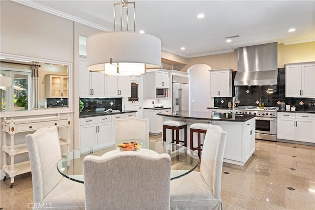 kitchen with white cabinetry, wall chimney exhaust hood, hanging light fixtures, premium appliances, and a kitchen island