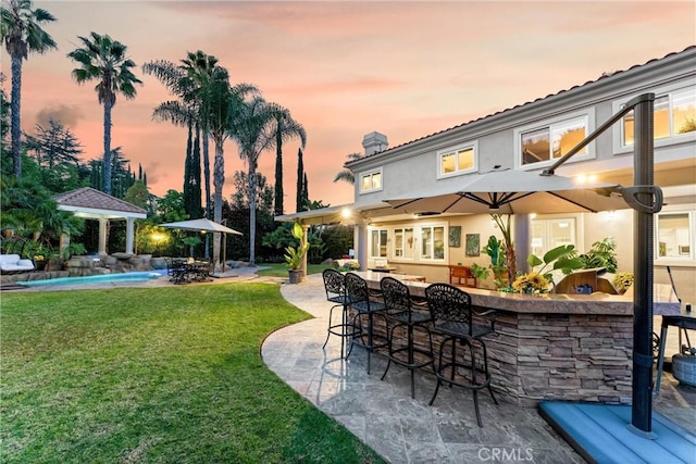 patio terrace at dusk featuring pool water feature, a yard, and an outdoor bar