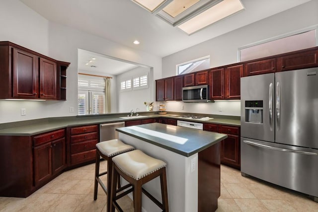 kitchen with light tile patterned flooring, appliances with stainless steel finishes, a kitchen island, a kitchen bar, and kitchen peninsula