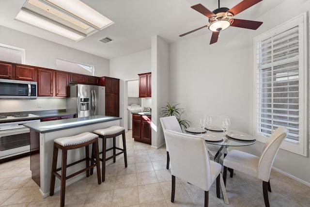 kitchen with light tile patterned floors, a center island, stainless steel appliances, and ceiling fan