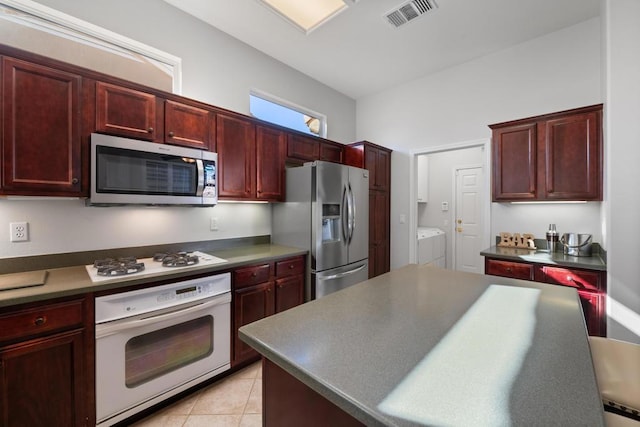 kitchen featuring light tile patterned floors, a center island, stainless steel appliances, and washer and clothes dryer