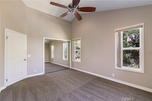 unfurnished bedroom featuring vaulted ceiling, dark carpet, multiple windows, and ceiling fan