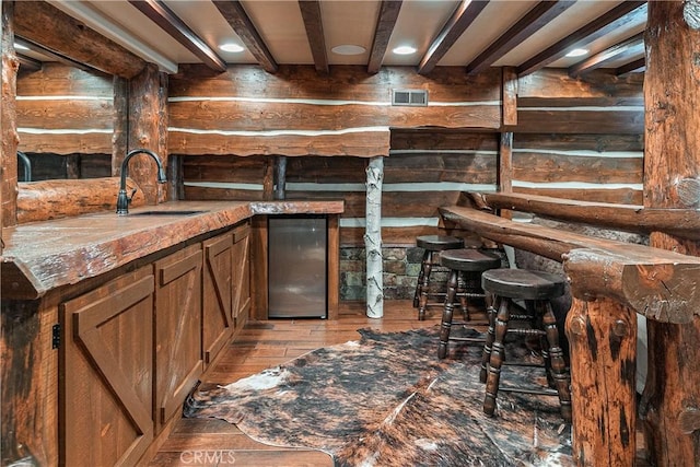 bar with stainless steel fridge, light hardwood / wood-style flooring, beam ceiling, and sink