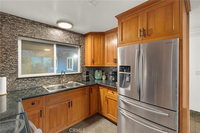 kitchen featuring dark stone counters, sink, stainless steel fridge, light tile patterned floors, and tasteful backsplash