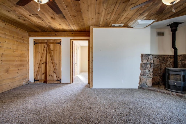 unfurnished living room featuring carpet flooring, a wood stove, wood walls, and wooden ceiling