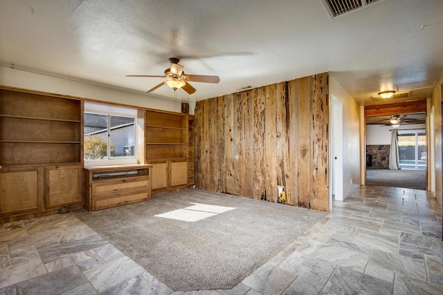 unfurnished living room with light carpet, ceiling fan, a healthy amount of sunlight, and wood walls