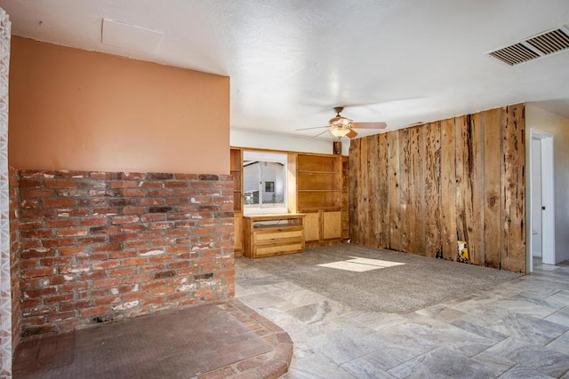 unfurnished living room with ceiling fan and wooden walls