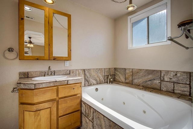 bathroom with tiled tub, ceiling fan, and vanity