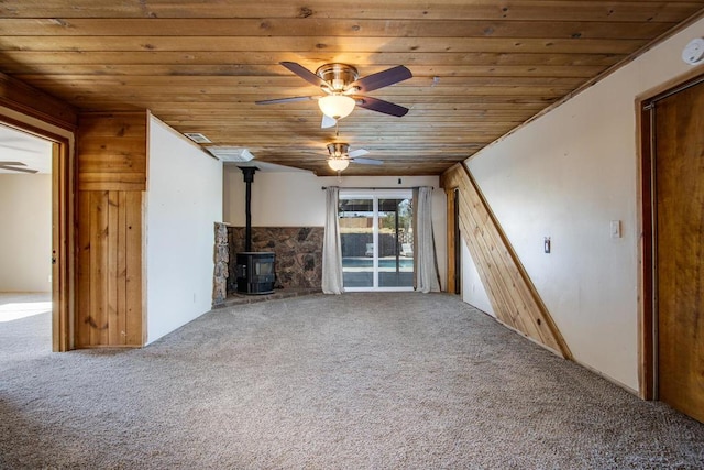 unfurnished living room with ceiling fan, a wood stove, carpet floors, and wood ceiling