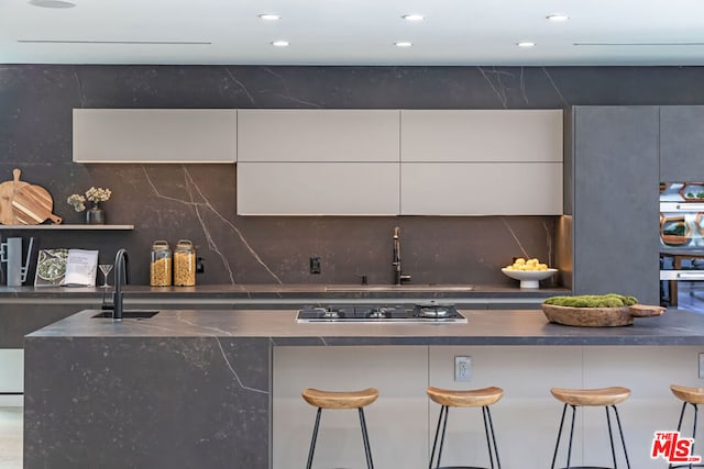 kitchen featuring white cabinetry, a kitchen breakfast bar, sink, and black gas cooktop