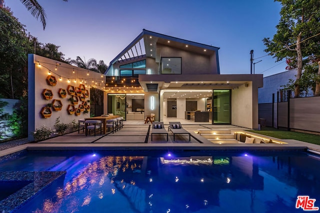 pool at dusk with an in ground hot tub, an outdoor kitchen, and a patio