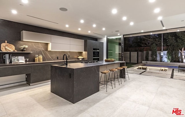 kitchen with a breakfast bar, white cabinetry, sink, backsplash, and a large island