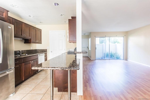 kitchen featuring stainless steel fridge, a kitchen breakfast bar, dark stone counters, light hardwood / wood-style flooring, and dishwasher