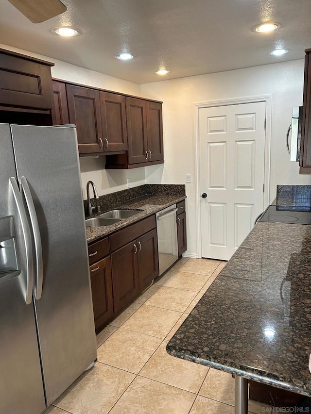 kitchen featuring dark brown cabinets, stainless steel appliances, dark stone countertops, and sink