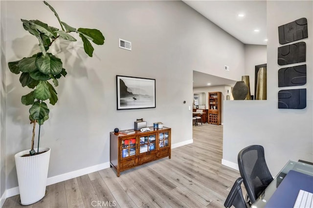 office area featuring a towering ceiling and light hardwood / wood-style flooring