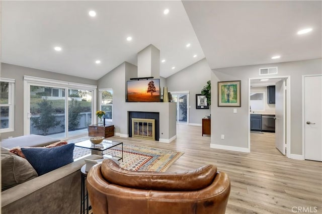 living room featuring a tile fireplace, lofted ceiling, and light hardwood / wood-style floors