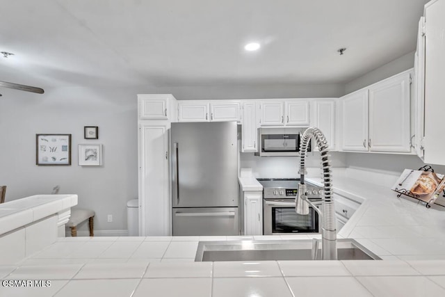 kitchen with white cabinetry, tile counters, stainless steel appliances, and sink