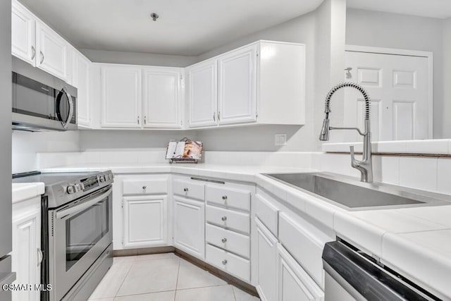 kitchen featuring tile countertops, white cabinets, sink, light tile patterned floors, and appliances with stainless steel finishes