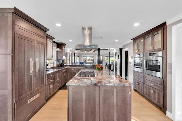 kitchen featuring light hardwood / wood-style floors, stainless steel appliances, light stone countertops, dark brown cabinetry, and a center island