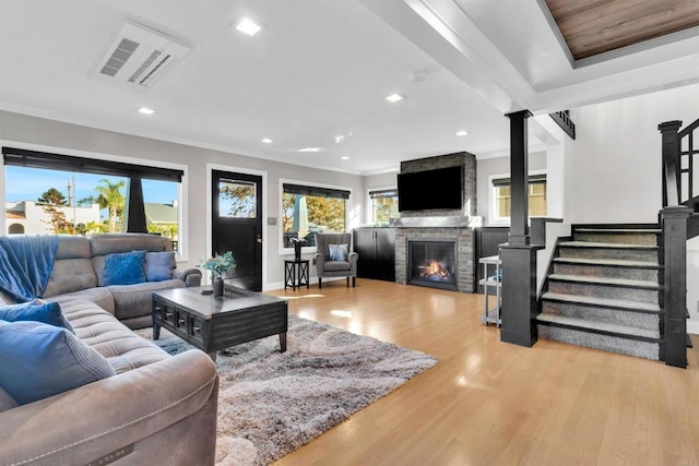 living room with light wood-type flooring, a stone fireplace, and ornamental molding