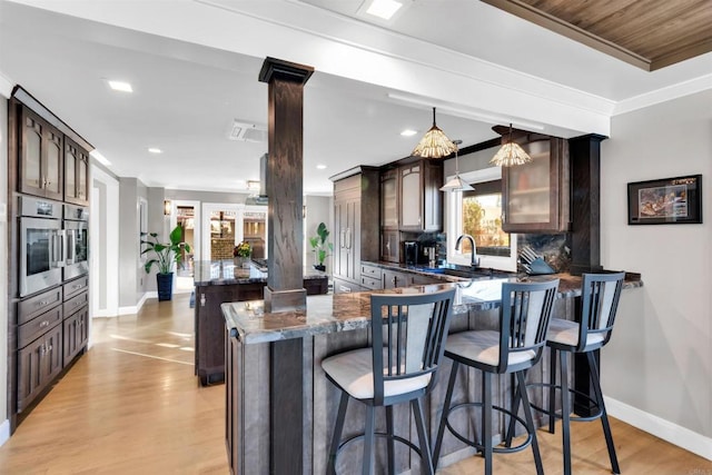 kitchen featuring decorative light fixtures, sink, oven, light hardwood / wood-style flooring, and dark brown cabinets