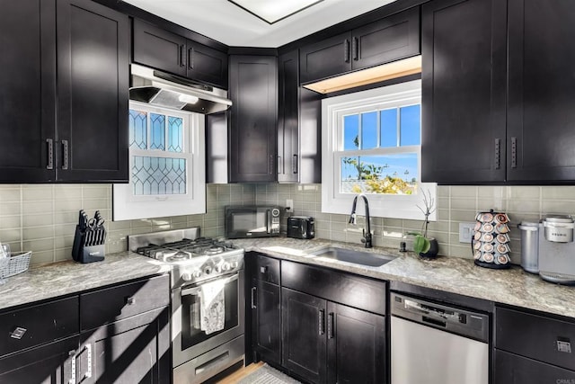 kitchen with tasteful backsplash, appliances with stainless steel finishes, sink, and light stone counters