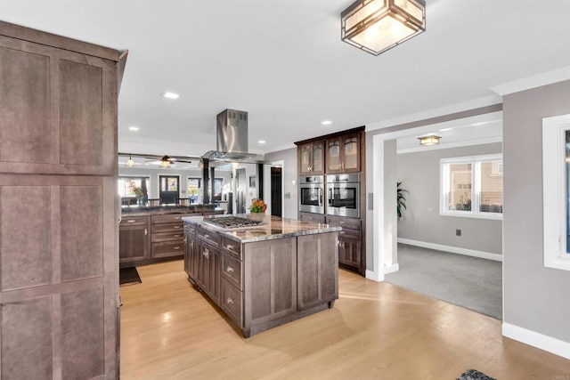 kitchen with light hardwood / wood-style floors, a kitchen island, appliances with stainless steel finishes, dark stone counters, and island range hood