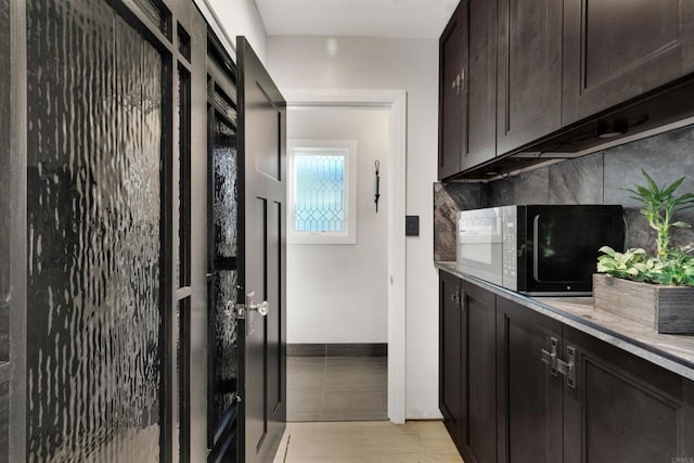 kitchen featuring black microwave, dark brown cabinets, light wood-type flooring, and tasteful backsplash