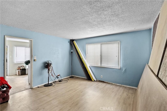 spare room with a textured ceiling, light wood-type flooring, and baseboards