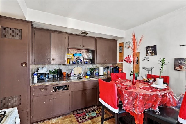 kitchen with dark brown cabinetry, stove, a sink, decorative backsplash, and dark countertops