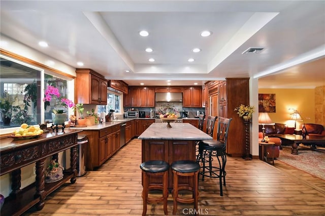 kitchen with dishwasher, a raised ceiling, light hardwood / wood-style flooring, a kitchen island, and a kitchen bar